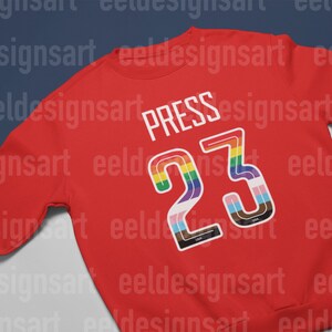 Puede incluir: Sudadera roja con el n&uacute;mero 23 en colores arco&iacute;ris y la palabra "PRESS" encima.