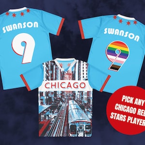 Op de afbeelding: Twee blauwe voetbalshirts met de naam "Swanson" en het nummer "9" op de rug. E&eacute;n shirt heeft een wit nummer en het andere een regenboognummer. Een derde shirt met een stadsbeeld en een trein op de voorkant zegt "Chicago" op de rug. Een rode cirkel met witte tekst zegt "Kies een willekeurige speler van de Chicago Red Stars!"