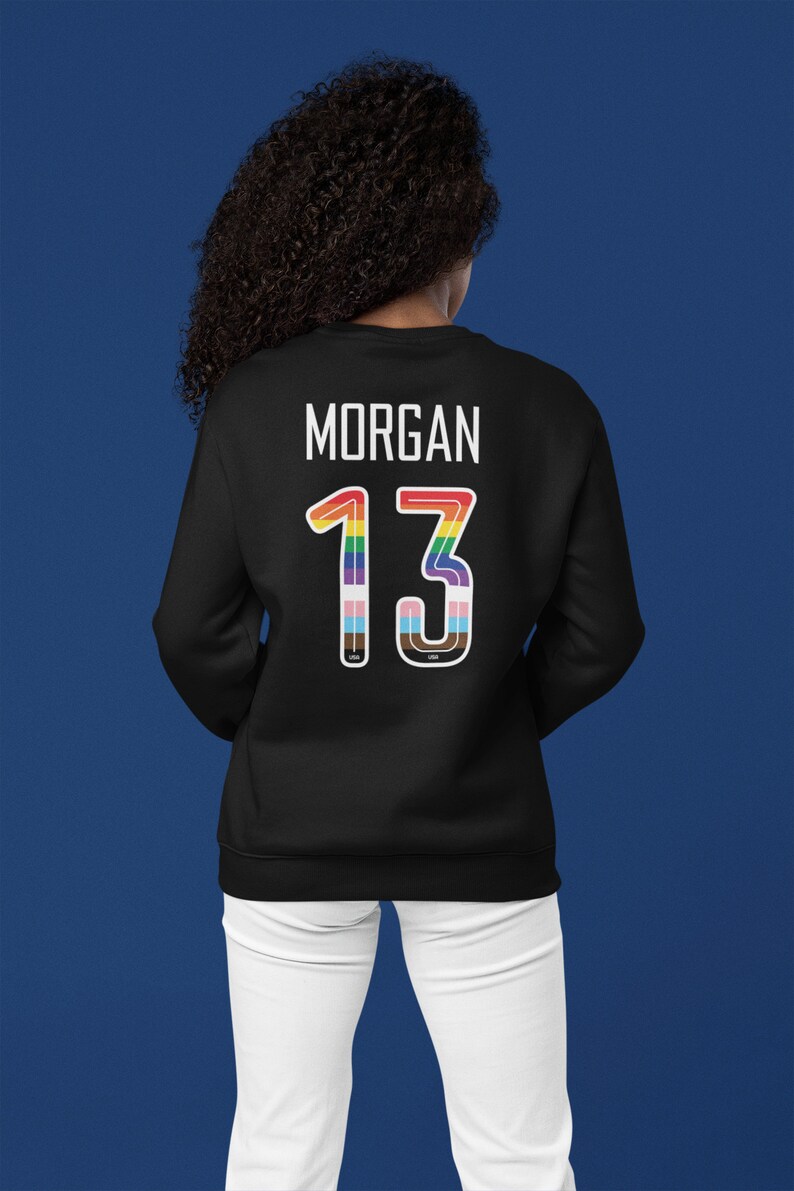 Puede incluir: Sudadera negra con el nombre "MORGAN" y el n&uacute;mero "13" en colores arco&iacute;ris en la espalda.
