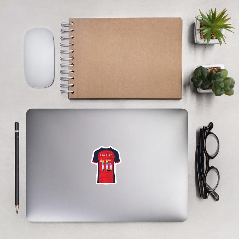 May include: A laptop computer with a sticker of a soccer jersey with the name "Lavelle" and the number "16" on the back. The jersey is red, white, and blue.