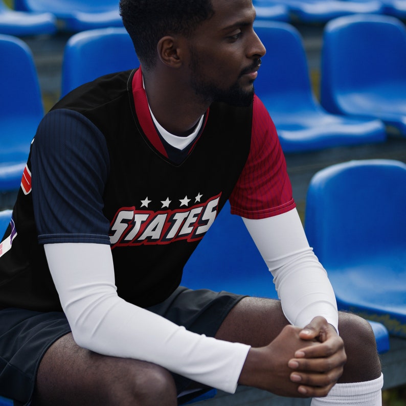 May include: A black and red baseball jersey with white stars and the word "STATES" in bold red letters. The jersey has a v-neck and long sleeves.