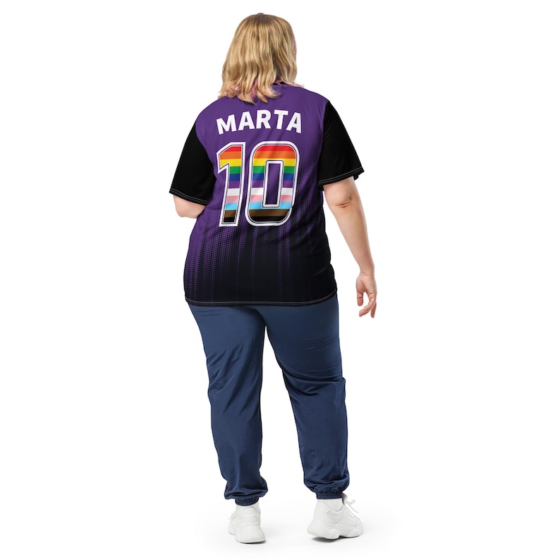 Op de afbeelding: Een paars en zwart shirt met een regenboogkleurig nummer 10 en de naam "Marta" op de rug.