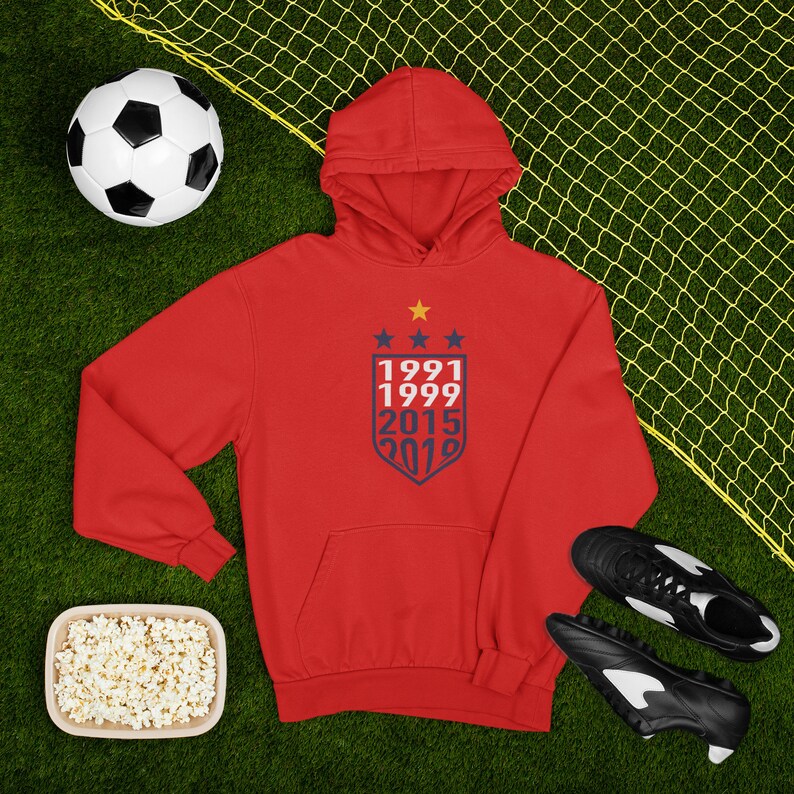 May include: Red hooded sweatshirt with a navy blue shield design featuring the years 1991, 1999, 2015, and 2019.