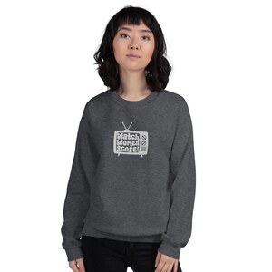 May include: A dark grey sweatshirt featuring a white graphic of a vintage television screen with the text "Watch Women Score!" inside.