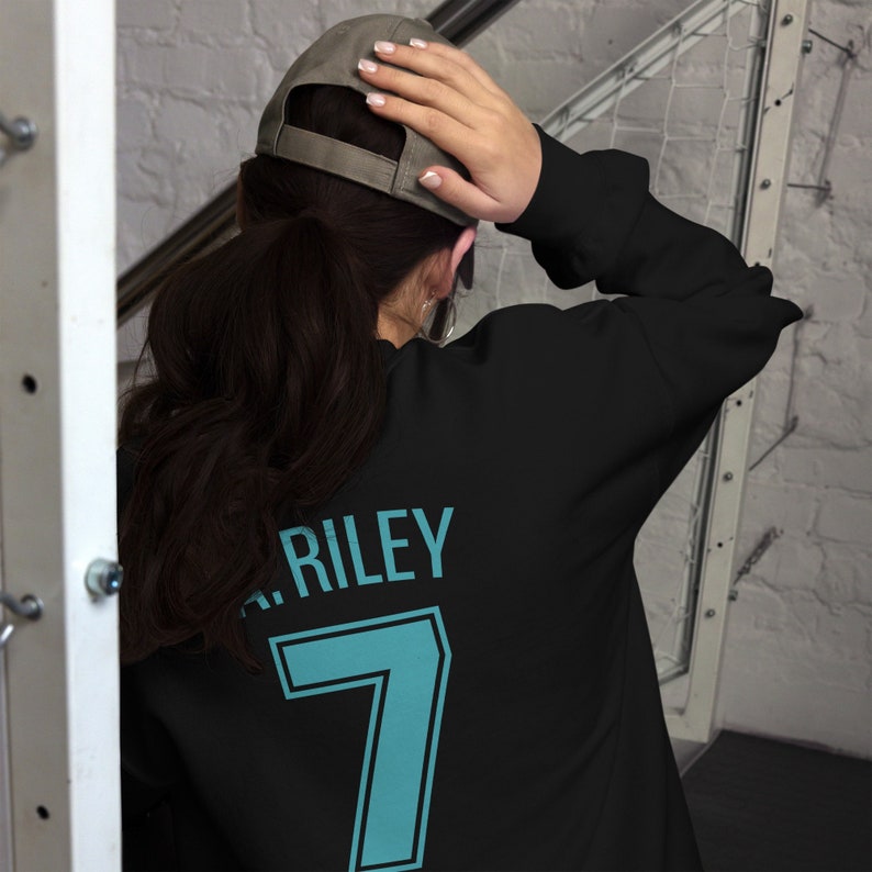 May include: Black sweatshirt with a teal blue number 7 and the name Riley printed on the back.