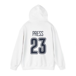 K&ouml;nnte beinhalten: Wei&szlig;er Kapuzenpullover mit dem Wort "PRESS" und der Nummer "23" in Marineblau auf der R&uuml;ckseite.