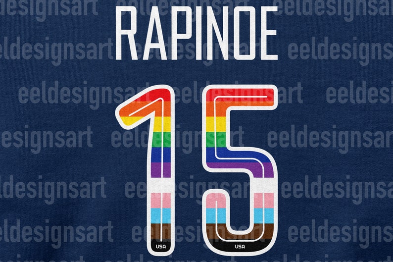 Puede incluir: Una camiseta azul con el nombre "RAPINOE" y el n&uacute;mero "15" en colores arco&iacute;ris. El n&uacute;mero est&aacute; contorneado en blanco y tiene una peque&ntilde;a bandera de EE. UU. en la parte inferior.