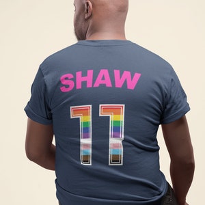 May include: A navy blue t-shirt with the name "SHAW" and the number "11" printed on the back. The number is in white with a rainbow stripe design.