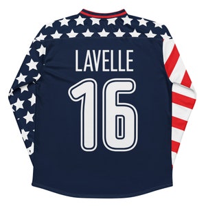 May include: A navy blue long-sleeved soccer jersey with white stars on the sleeves and a red, white, and blue stripe on the right sleeve. The jersey has the name "LAVELLE" and the number "16" printed on the back in white.
