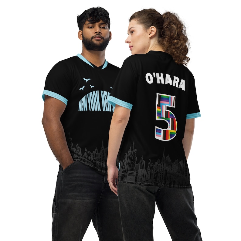 K&ouml;nnte beinhalten: Zwei schwarze Fu&szlig;balltrikots mit einem Stadtbild-Design. Ein Trikot hat den Text "NEW YORK NEW" und das andere hat den Text "O'HARA 5" mit einer Nummer 5 aus Flaggen.