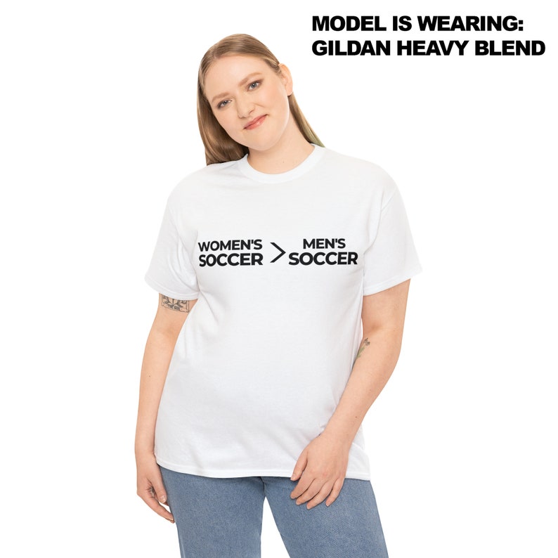 May include: White t-shirt with the text "Women's Soccer > Men's Soccer" printed on the front.
