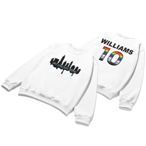 May include: White sweatshirt with a black silhouette of the New York City skyline and the text "NEW YORK/NEW JERSEY" on the front. The back of the sweatshirt has the text "WILLIAMS" and the number "10" in rainbow colors.