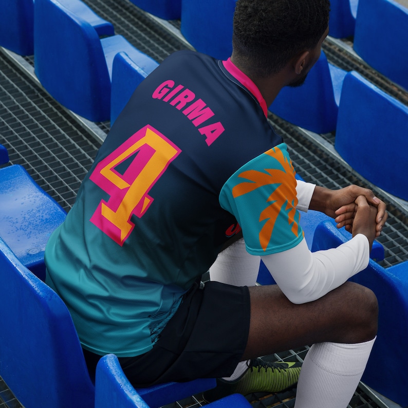 May include: A person wearing a blue, teal, and orange soccer jersey with the number "4" and the name "GIRMA" on the back. The jersey has a palm tree design on the sleeve.