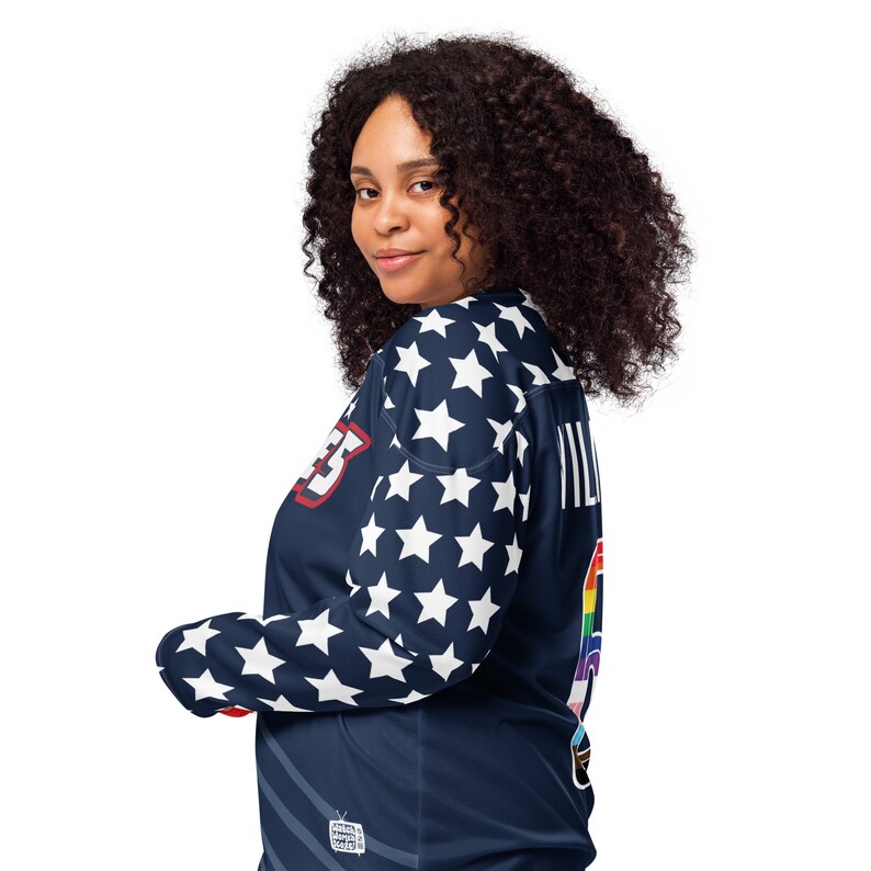 May include: A navy blue long-sleeved shirt with white stars, a rainbow patch, and the text "VILLAGES" on the back. The shirt has a red, white, and blue patch on the front with the text "VILLAGES".