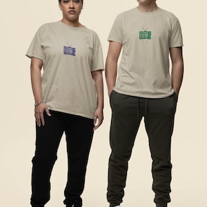 May include: Two people wearing sand colored t-shirts with a vintage television graphic. The television graphic on the left shirt is blue and the graphic on the right shirt is green. Both people are wearing black pants and white sneakers.