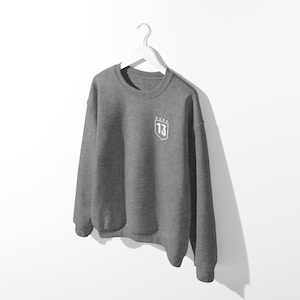 May include: A gray sweatshirt with a white embroidered shield on the left chest. The shield has the number "13" and five stars above it.