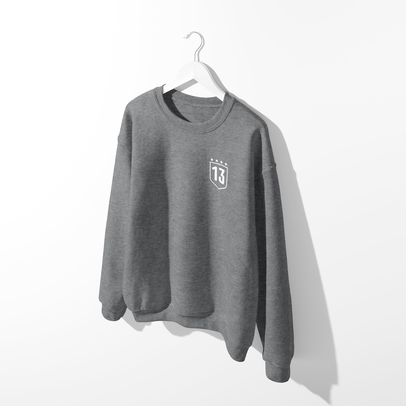 May include: A gray sweatshirt with a white embroidered shield on the left chest. The shield has the number "13" and five stars above it.