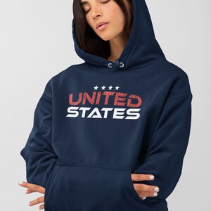 Op de afbeelding: Een marineblauwe hoodie met een witte en rode grafische print die "UNITED STATES" zegt met vijf sterren boven het woord "UNITED".