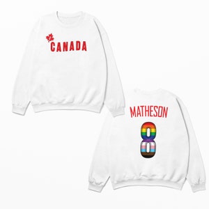 May include: White sweatshirt with "CANADA" printed on the front in red with a red maple leaf. The back of the sweatshirt has "MATHESON" printed in red with a rainbow number "8" printed below.