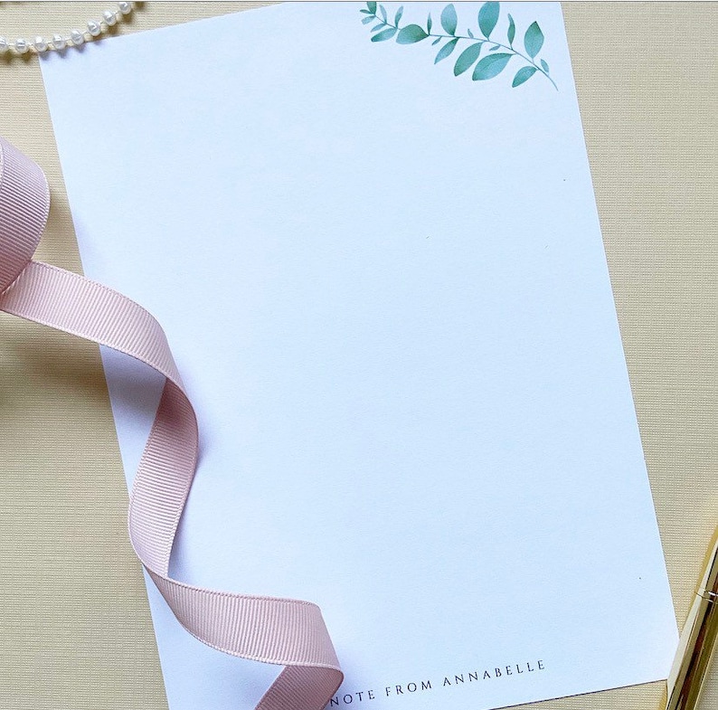 May include: A white stationery notecard with a green leafy branch design in the top right corner. The text "NOTE FROM ANNABELLE" is printed in black at the bottom of the card.