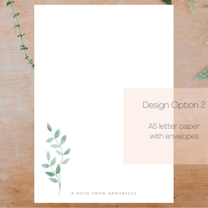 May include: A white card with a green watercolor leaf design. The card has the text "A Note From Annabelle" at the bottom. The card is on a wooden surface with green leaves. The text "Design Option 2" and "A5 letter paper with envelopes" is on a peach background.