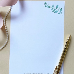 May include: A white stationery notecard with a green leafy branch design in the top right corner. The text "A note from Annabelle" is printed at the bottom of the card.