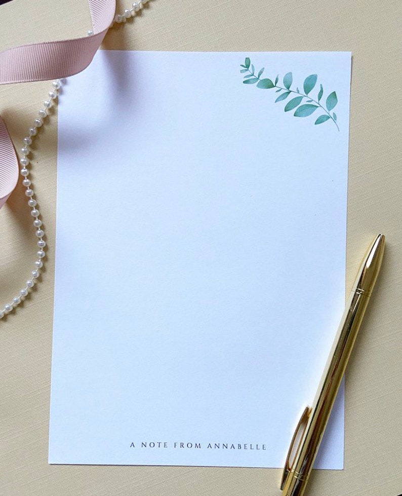 May include: A white stationery notecard with a green leafy branch design in the top right corner. The text "A note from Annabelle" is printed at the bottom of the card.