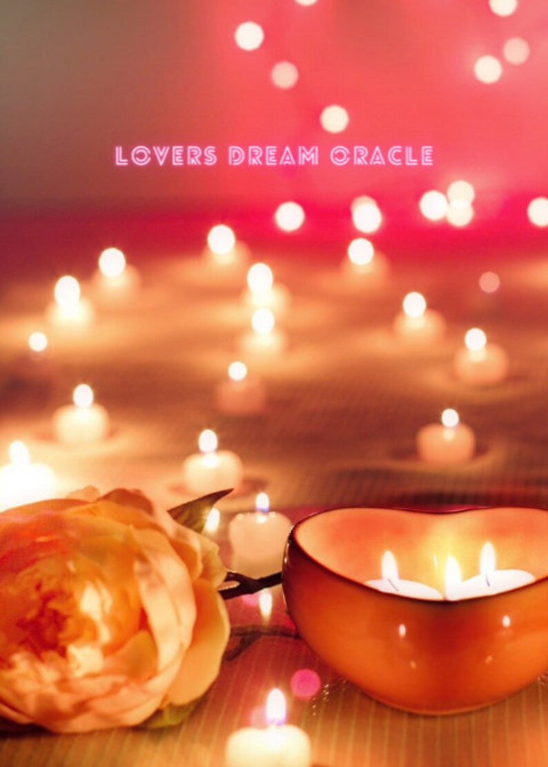 May include: A heart-shaped ceramic bowl with three lit candles inside, surrounded by a single orange rose and several small lit candles on a wooden surface. The text "LOVERS DREAM ORACLE" is displayed in pink neon letters above the bowl.