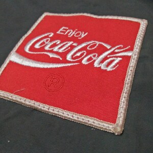 Może przedstawiać: Czerwona naszywka z tkaniny z białym haftem z napisem "Enjoy Coca-Cola" i symbolem znaku towarowego.