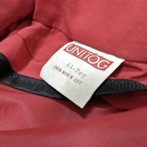 Może przedstawiać: Czerwony materiał z białą metką, na kt&oacute;rej widnieje napis "UNITOG" i "44-Reg", a pod nim tekst "UNION MADE IN USA".
