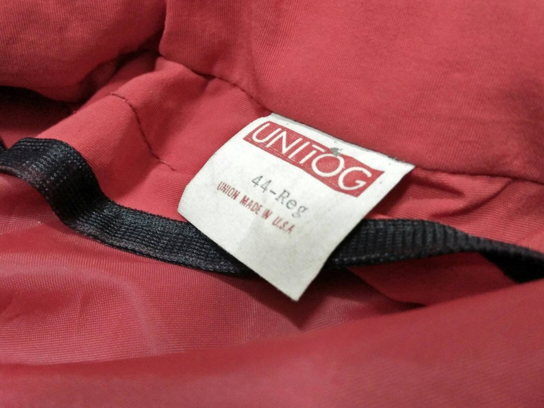 Może przedstawiać: Czerwony materiał z białą metką, na kt&oacute;rej widnieje napis "UNITOG" i "44-Reg", a pod nim tekst "UNION MADE IN USA".