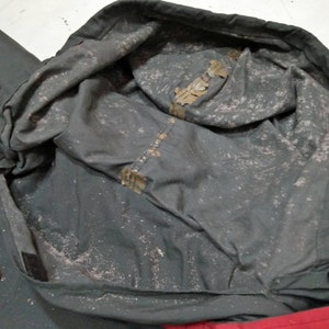 Może przedstawiać: Zbliżenie na wnętrze zielonej kurtki z kapturem. Kaptur jest podszyty białym materiałem i ma sznurek. Kurtka jest wykonana z wodoodpornego materiału.