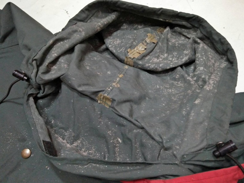 Może przedstawiać: Zbliżenie na wnętrze zielonej kurtki z kapturem. Kaptur jest podszyty białym materiałem i ma sznurek. Kurtka jest wykonana z wodoodpornego materiału.