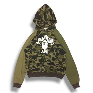 May include: A green, brown, and white camouflage hooded sweatshirt with a white "A Bathing Ape" logo on the front.