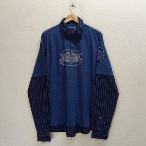 May include: A blue long-sleeve shirt with a striped pattern on the sleeves. The shirt features a graphic of a motorcycle with the text "The Breakaway One" and "But I wear never leave me be".