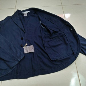 May include: A navy blue blazer with a single button closure and a large pocket on the inside. The blazer has a relaxed fit and is made of a lightweight fabric.