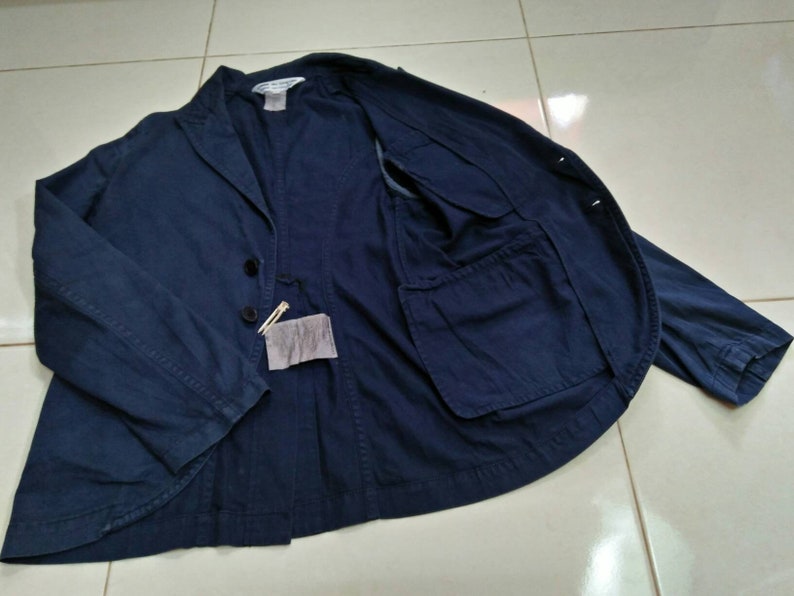 May include: A navy blue blazer with a single button closure and a large pocket on the inside. The blazer has a relaxed fit and is made of a lightweight fabric.