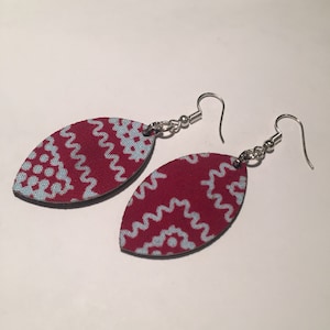 May include: A pair of red and blue patterned earrings with silver hooks. The earrings are shaped like a leaf and have a white and blue geometric design.