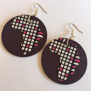 May include: A pair of brown leather earrings with a pink and white patterned cutout of the continent of Africa.