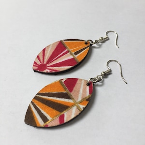May include: A pair of dangle earrings with a geometric pattern in shades of orange, pink, brown, and gold. The earrings are made of fabric and have silver hooks.