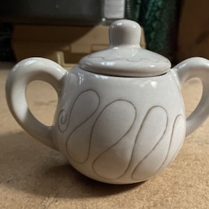 May include: A white ceramic sugar bowl with a lid. The bowl has a swirl design in brown glaze.