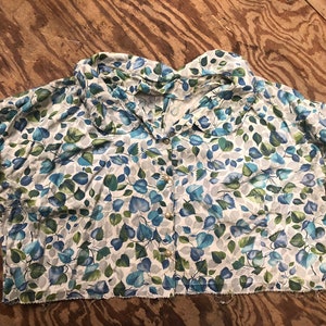 May include: A white, short-sleeved blouse with a blue and green leaf pattern. The blouse has a collar and buttons down the front.