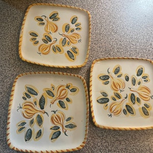May include: Three square ceramic plates with a yellow and brown onion design on a white background. The plates have a brown and yellow border.