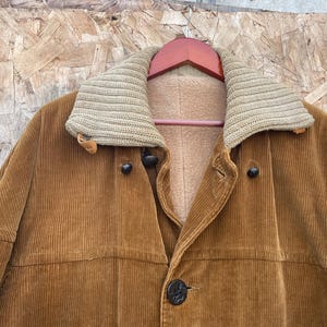 May include: A corduroy jacket in a warm brown hue, featuring a knitted collar and a soft, light-colored lining. The jacket has a button closure and a classic design, suitable for outerwear.