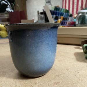 May include: A blue and grey ceramic planter with a rounded bottom and a wide opening. The planter is made of glazed ceramic and has a subtle ombre effect.