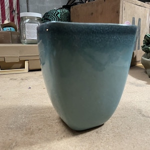 May include: A light blue ceramic planter with a textured, speckled finish. The planter has a rounded bottom and a wide, open top.
