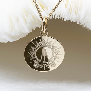 May include: A gold necklace with a round pendant featuring an engraved design of a stylised hand with a mandala pattern around it.