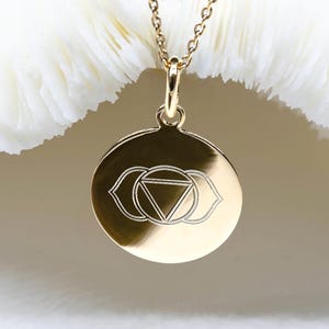 Peut inclure: Collier en or avec un pendentif rond gravé d'un symbole du troisième œil, également connu sous le nom de chakra Ajna.