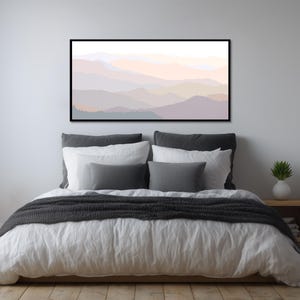 May include: A rectangular wall art print featuring a layered mountain landscape in soft, muted pastel tones of peach, lavender, and grey. The artwork is enclosed in a thin black frame and depicts overlapping mountain silhouettes with a hazy, atmospheric effect.