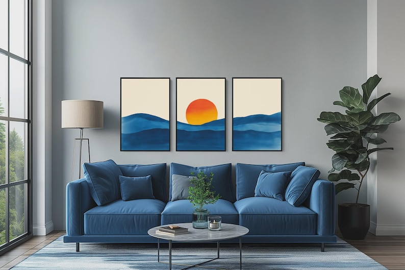 May include: Three framed abstract art prints with a blue and orange color scheme. The prints depict a stylized sunset over a blue ocean. The prints are hanging on a gray wall above a blue sofa.